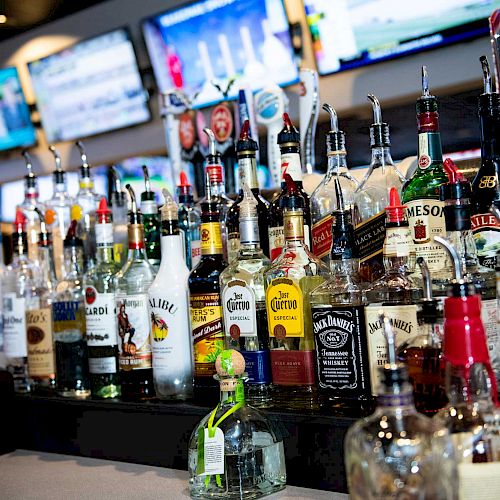 A bar counter with various liquor bottles and multiple televisions displaying sports in the background can be seen in this image.