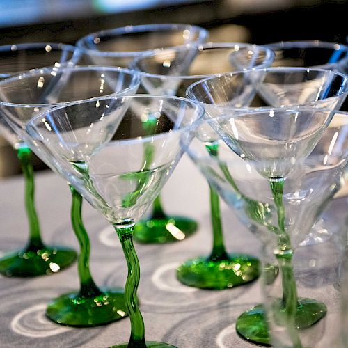 The image shows several clear martini glasses with green twisted stems arranged on a patterned surface.