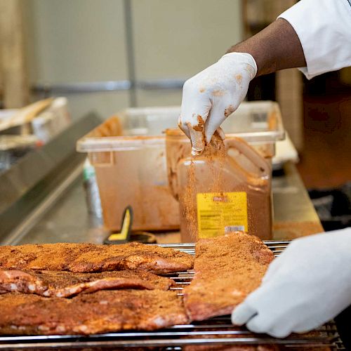 A person wearing gloves is seasoning ribs with spices in a kitchen.