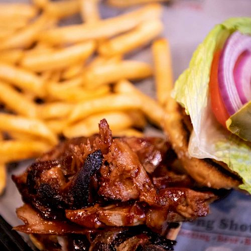 The image shows a meal of French fries, a pile of grilled meat, and an open-faced burger with lettuce, tomato, red onion, and a pickle.