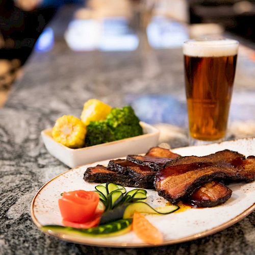 The image shows a meal with grilled beef slices, garnished vegetables, a side of broccoli and cauliflower, and a pint of beer on a table.