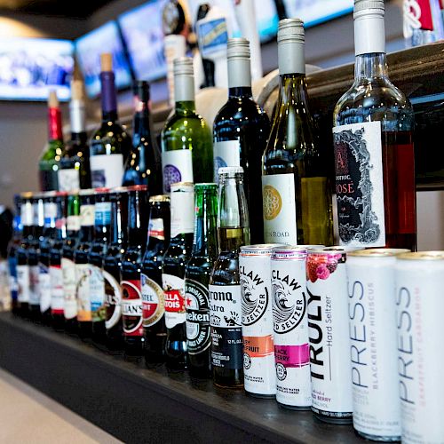 The image showcases a variety of alcoholic beverages, including wine bottles, beer bottles, and canned drinks, neatly arranged on a bar counter.