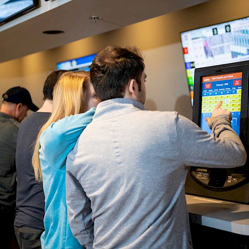 Several people are interacting with betting machines in a setting with multiple TV screens showing sports and odds.