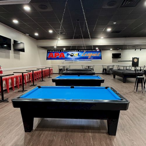 The image shows a pool hall with several pool tables, a sign saying "APA Pool Leagues," and red bar stools along the wall.