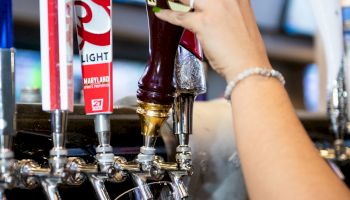 A person is pouring beer from a tap into a glass at a bar, with other beer taps visible, including ones labeled Coors and Blue Moon.