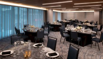The image shows an elegant banquet hall with round tables set with dinnerware and black napkins, ready for an event or reception.