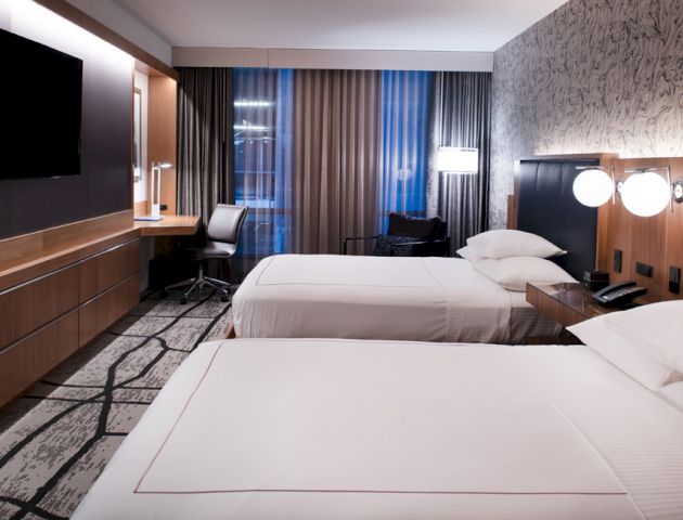 The image shows a modern hotel room with two beds, a wall-mounted TV, a desk with a chair, stylish lighting, and contemporary decor, ending the sentence.