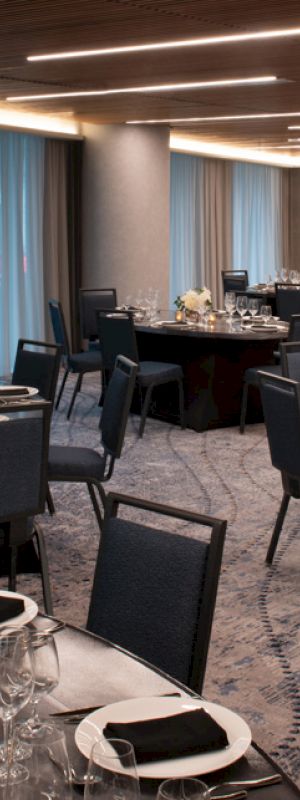 An elegant dining area with round tables set with plates, glasses, napkins, and centerpieces. Modern decor and ambient lighting enhance the setting.