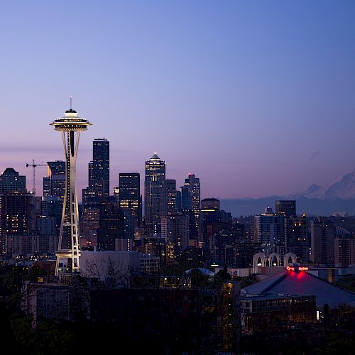 City skyline at dusk with illuminated Space Needle and Mount Rainier in the background.